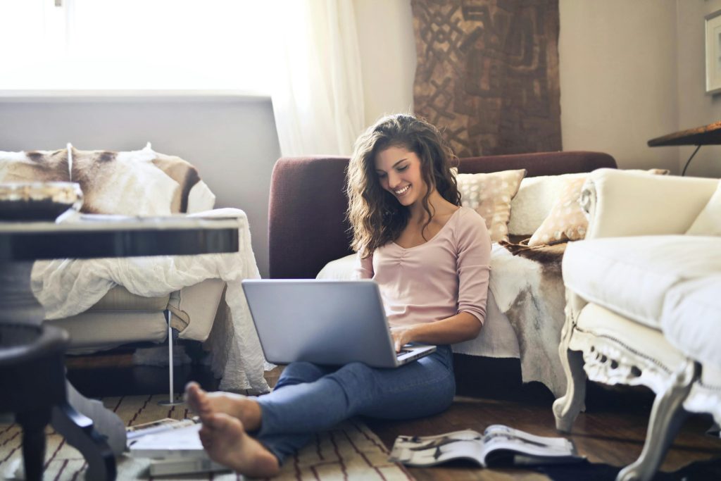pexels-photo-3769717-3769717 Smiling woman using a laptop seated on the floor in a cozy living room, working remotely.